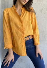 Camisa color mostaza con bordado de flores, cuello con volados, mangas largas abullonadas y cierre frontal con botones.