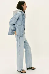 Cazadora de denim oversize con capucha gris desmontable, cuello camisero, cierre frontal con botones metálicos y bolsillos delanteros de plastrón.