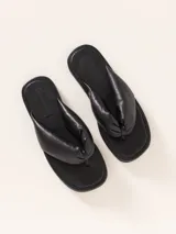 Sandalia plana tipo ojota de cuero vacuno, color negro, con tira ancha y acolchada que pasa entre los dedos.