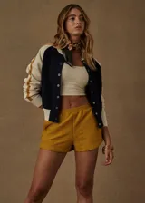 Campera bomber azul marino con mangas color crema con rayas mostaza. Tiene cuello, puños y ruedo acanalados, cierre frontal con botones a presión y corte holgado.