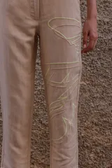 Pantalón chino color beige de lino y viscosa, con bordado de palmeras en verde claro. Tiene tiro medio-alto, pierna recta y bolsillos laterales y traseros.