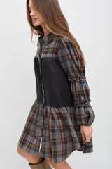 Vestido midi de corte holgado con diseño combinado en tela escocesa gris y naranja y panel central negro. Presenta cuello mao, cierre frontal con botones, mangas largas abullonadas con detalles de volados y puños elásticos.