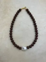 Collar artesanal compuesto por cuentas de piedra volcánica en diversos tonos y tamaños, con una perla natural de río como dije central y cierre metálico dorado.