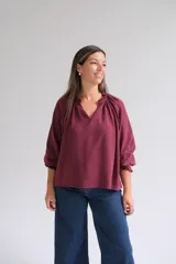 Blusa bordó de corte holgado, con escote en V y cuello fruncido. Presenta mangas tres cuartos con puños elásticos y detalles de volados.