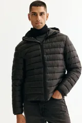 Campera puffer liviana negra con cuello elevado y capucha, cierre frontal con protección para el mentón, bolsillos laterales con cierre y bolsillos interiores abiertos. Tiene un corte ajustado que realza la silueta.