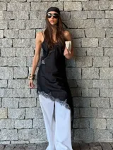 Vestido tipo slip dress negro, con tirantes finos y detalles de encaje en el escote y en el dobladillo asimétrico.