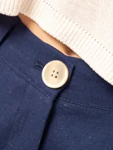 Pantalón de lino color beige, de tiro alto, pierna ancha y levemente acampanada. Tiene pinzas delanteras, elástico en la pretina trasera, cierre delantero y broche interno, bolsillos laterales y dobladillo invisible.