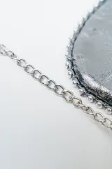 Cartera negra de cuero con solapa y detalles de tachas plateadas. Incluye una correa de cadena plateada.