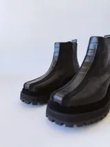 Botas negras de cuero con caña baja, cierre lateral con cremallera y suela track.