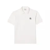 Chomba Lacoste de piqué color blanco, de manga corta, con cuello camisero y cierre frontal de dos botones. Cuenta con el logotipo de la marca bordado en el pecho junto con el texto "Lacoste Paris".