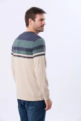 Remera de manga larga con cuello redondo, diseño a rayas horizontales en beige, marrón y azul marino, con finas líneas decorativas en rojo, azul y verde. Incluye un pequeño logo bordado en el pecho.