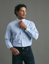 Camisa de vestir de manga larga con diseño de rayas verticales finas en color celeste y blanco. Presenta cuello clásico, cierre frontal con botones y un bolsillo en el pecho.