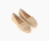 Mocasín de cuero gamuzado color avena, con detalle de flecos en la capellada y un lazo frontal con herrajes metálicos dorados. Cuenta con interior forrado en cuero y suela de goma flexible.