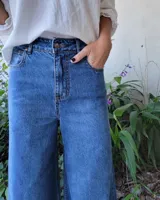 Pantalón de jean color beige, de corte recto y tiro alto, con ruedo deshilachado y cierre frontal con botón y cremallera.