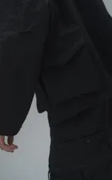 Campera técnica liviana de microfibra negra con acabado mate, capucha ajustable, cierre frontal oculto bajo solapa, bolsillos frontales con solapa y cordón ajustable en la cintura.