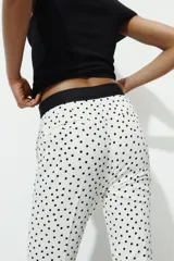 Pantalón de tiro medio con estampado de lunares negros sobre fondo blanco. Presenta bolsillos delanteros, falsos bolsillos traseros, aberturas laterales en el bajo y cierre frontal con cremallera, botón y gancho.