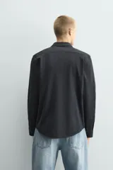 Camisa de corte relajado confeccionada en tejido de algodón con textura. Presenta cuello italiano, manga larga con puños abotonados y cierre frontal mediante botonadura.