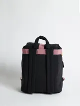 Mochila acolchada de nylon color negro con correas y detalles en rosa pálido. Presenta un cierre principal tipo solapa con hebilla de plástico negra y una cinta colgante con el texto "rusty" en color verde menta.