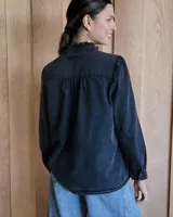 Camisa de jean azul con cuello alto con volados y volados en el frente.