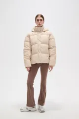 Campera puffer color beige con diseño capitoneado, capucha integrada y cierre frontal oculto. Presenta bolsillos laterales y un corte holgado.