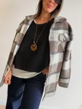 Sobrecamisa de paño con diseño a cuadros en tonos marrones, grises y blancos. Presenta cuello clásico, cierre frontal con botones y bolsillos delanteros con tapa.