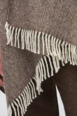 Ruana de lana sin teñir en tono marrón jaspeado, con diseño envolvente y terminaciones de flecos en color crudo.