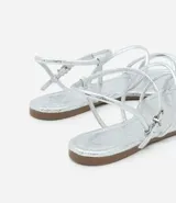 Sandalia plana dorada con tiras finas y cierre con hebilla en el tobillo.