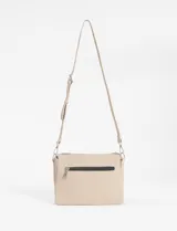 Bandolera de tamaño compacto en color beige, confeccionada en cuero vegano. Presenta un diseño con pespuntes verticales visibles, cierre superior y correa larga ajustable y extraíble. Incluye un pequeño aplique metálico decorativo en la parte inferior frontal.