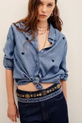 Camisa de lyocell color azul con efecto deslavado y pequeños bordados de corazones oscuros distribuidos por toda la prenda. Cuenta con cuello camisero, cierre frontal de botones y mangas largas.