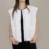 Chaleco holgado sin mangas, color blanco, con bolsillos frontales con solapa y cierre de cremallera metálica.