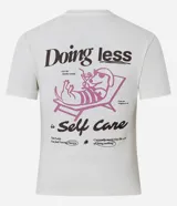Remera de algodón con cuello redondo, mangas cortas y estampa en la espalda con diseño de un perro descansando en una reposera y la frase "Doing less is Self Care".