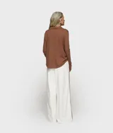 Blusa cruzada de punto de algodón orgánico color marrón, con cuello, cierre de botón, puños con abertura y monograma bordado en la manga izquierda. Tiene bajo recto y aberturas laterales.