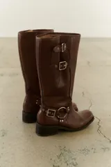 Bota de cuero negra de caña alta con herrajes plateados, hebillas y arnés.