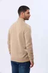 Buzo de punto color beige, con cuello alto y cierre frontal con cremallera y solapa de gamuza con botón. Presenta un tejido texturizado en el cuerpo y mangas lisas.