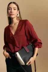 Blusa de satén color bordó con escote en V, detalle de solapas con volados en el frente y mangas largas con puños abotonados.