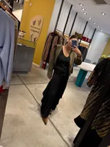 Pantalón de corte amplio y fluido, color gris con acabado satinado, con cintura elástica y lazo ajustable. Presenta un diseño con paneles laterales que aportan volumen y movimiento.