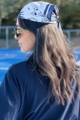 Pañuelo de cabeza tipo bandana, de color blanco con estampado lineal en azul marino que representa figuras arquitectónicas y detalles geométricos.