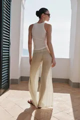 Pantalón de pierna ancha y tiro medio, confeccionado en tejido con textura arrugada. Presenta una cintura elástica destacada por un detalle de tejido en crochet a tono.