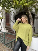 Sweater de punto color verde lima, con diseño de textura acanalada horizontal y costura central vertical decorativa. Presenta cuello redondo, mangas largas con puños ajustados y un corte asimétrico con el frente más corto que la espalda.