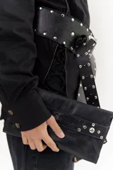 Sobre de cuero negro con solapa, cierre magnético y muñequera con tachas plateadas.