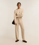 Pantalón wide leg de punto color beige, de tiro medio con cintura elástica ancha de rib, lazo ajustable con punteras metalizadas y costuras verticales decorativas.