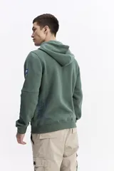 Campera con capucha y cierre frontal, color crema, con bolsillo canguro. Presenta un estampado de texto en el pecho y detalles en el puño.