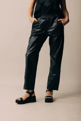 Pantalón estilo babucha de cuero negro, con cintura ancha y elastizada, y corte recto en las piernas.