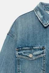 Sobrecamisa crop de denim con cuello solapa, manga larga con puños, bolsillos frontales con solapa y cierre de botones ocultos. Presenta un diseño con bajo deshilachado y detalles de roturas.