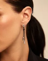 Aros largos colgantes de metal plateado con forma de esfera en la parte superior, tira de cuero negro con nudo y dije plateado en forma de rombo.