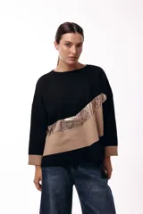 Sweater de punto con diseño de bloques de color en diagonal, combinando negro, beige y una franja central con textura metalizada. Presenta cuello redondo, mangas largas con puños en contraste y un corte holgado.