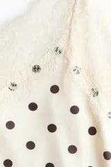 Vestido midi de satén blanco con estampado de lunares negros, escote en V con ribetes de encaje, breteles finos y bajo asimétrico con detalles de encaje.