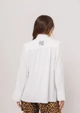 Camisa blanca de cuello redondo con frunces, abotonada y de manga larga con puño abierto.