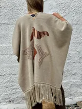Ruana abierta de lana merino en color beige, con diseño de corte amplio y terminaciones con flecos en el ruedo.