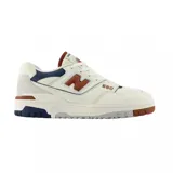 Championes urbanos New Balance modelo 550, con diseño retro inspirado en el básquetbol. Presentan una combinación de cuero perforado y gamuza en tonos blanco, crema, azul marino y detalles en color tostado. Cuentan con suela de goma resistente y logo lateral característico.